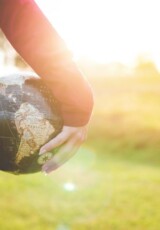 person holding black and brown globe ball while standing on grass land golden hour photography